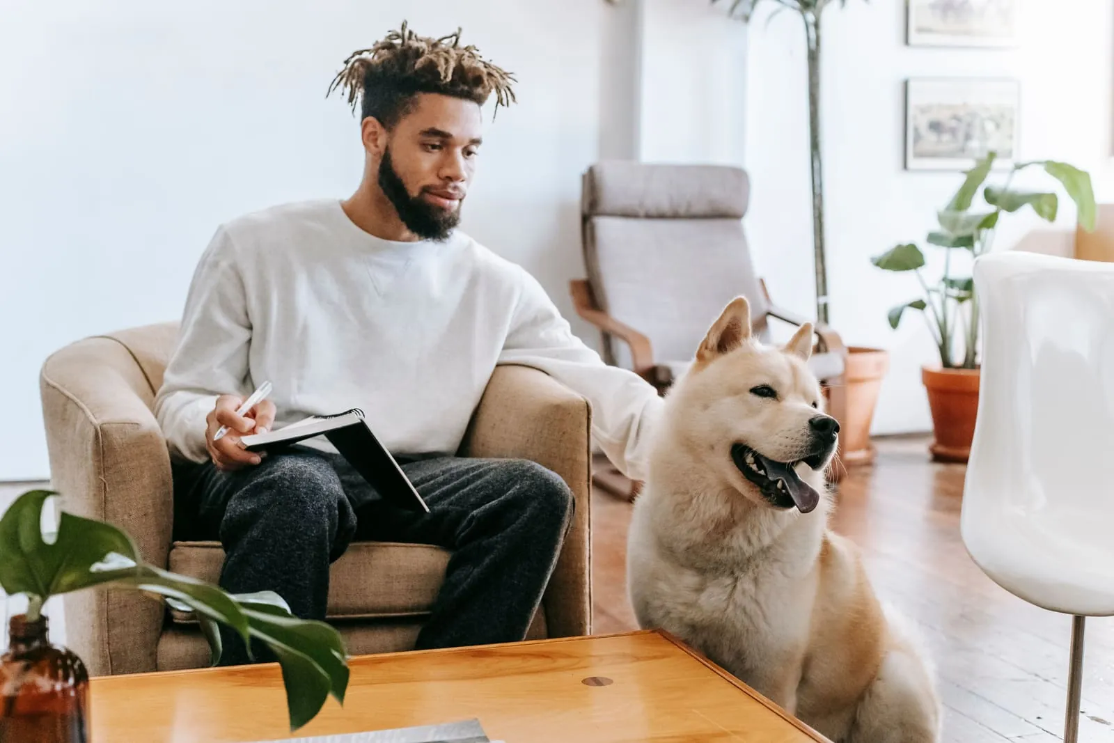 Man taking notes in a notebook next to his dog, planning out a new treatment conversation with the vet